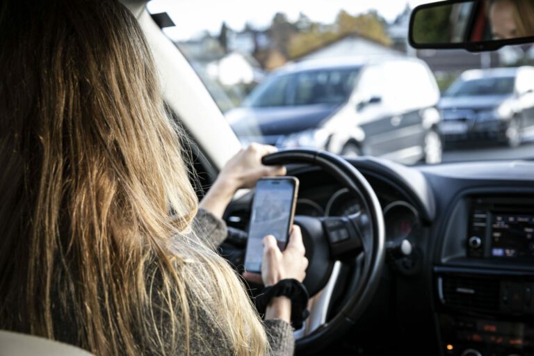 Illustrasjonsbilde: Bilde av kvinne som sitter i førersetet på en bil og holder en mobiltelefon i hånden